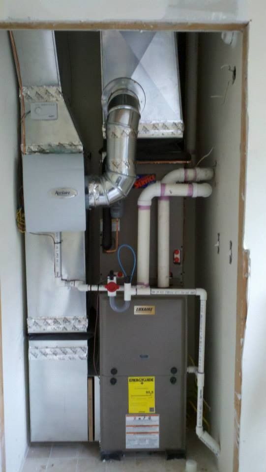 Furnace and HVAC components installed in a closet. Gray metal furnace with ductwork and plumbing.