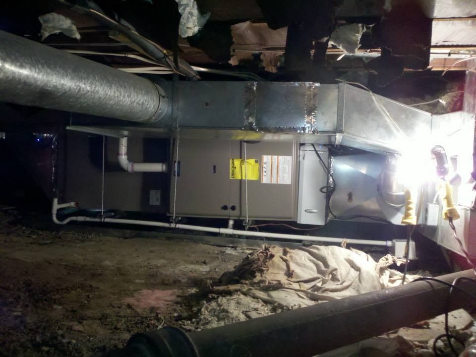 HVAC unit in a dark basement with ductwork, piping, and insulation.