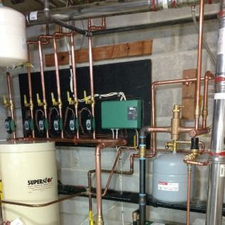 Copper pipes, water tanks, and green control box for a heating system in a basement.