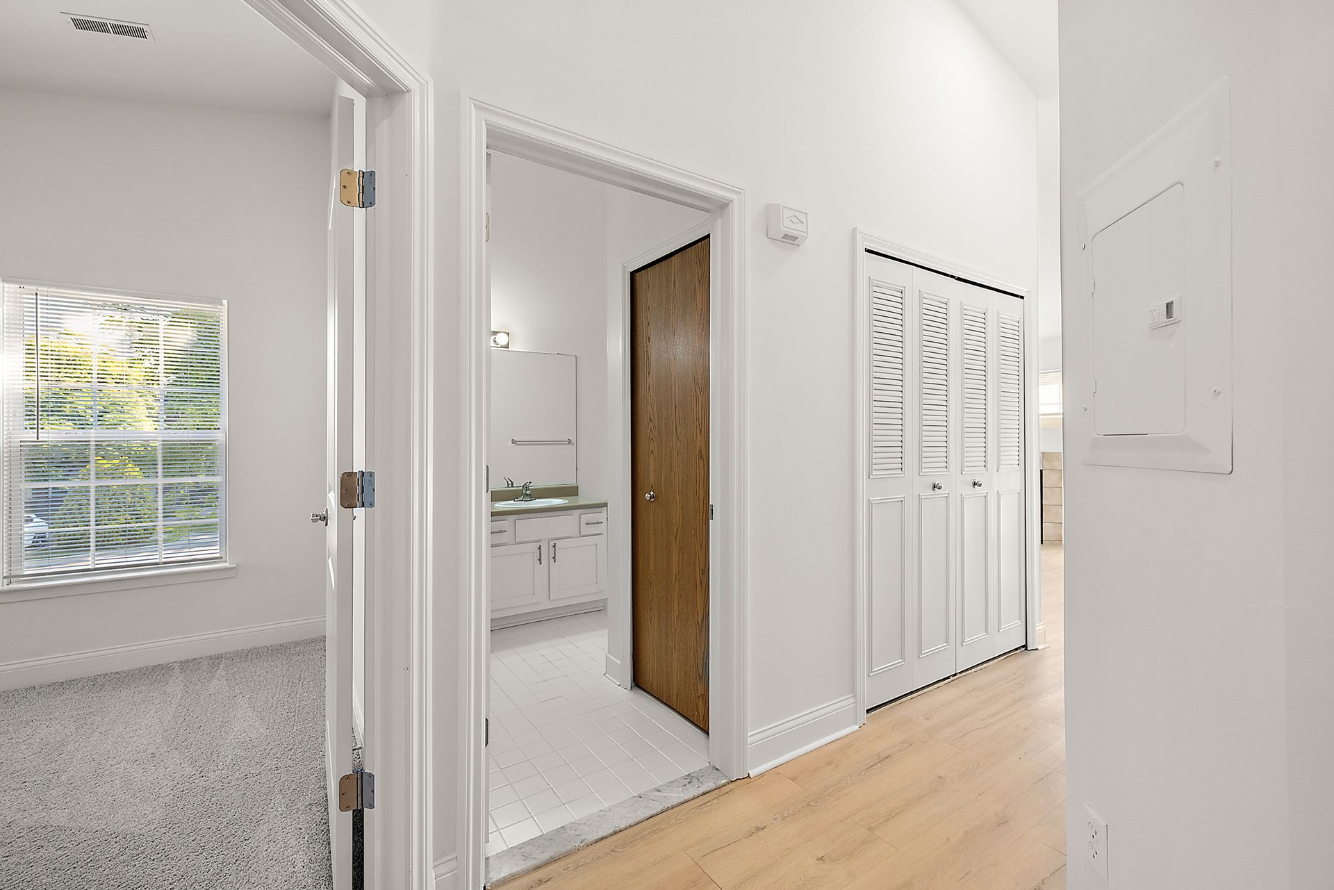 A hallway leading to a bathroom and a closet in a house.