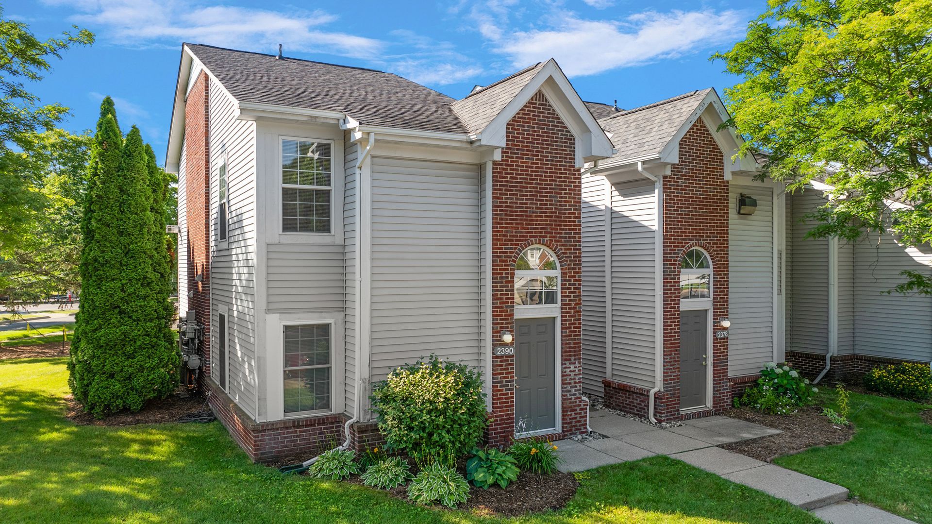 A small white house with a brick facade is sitting on top of a lush green lawn.