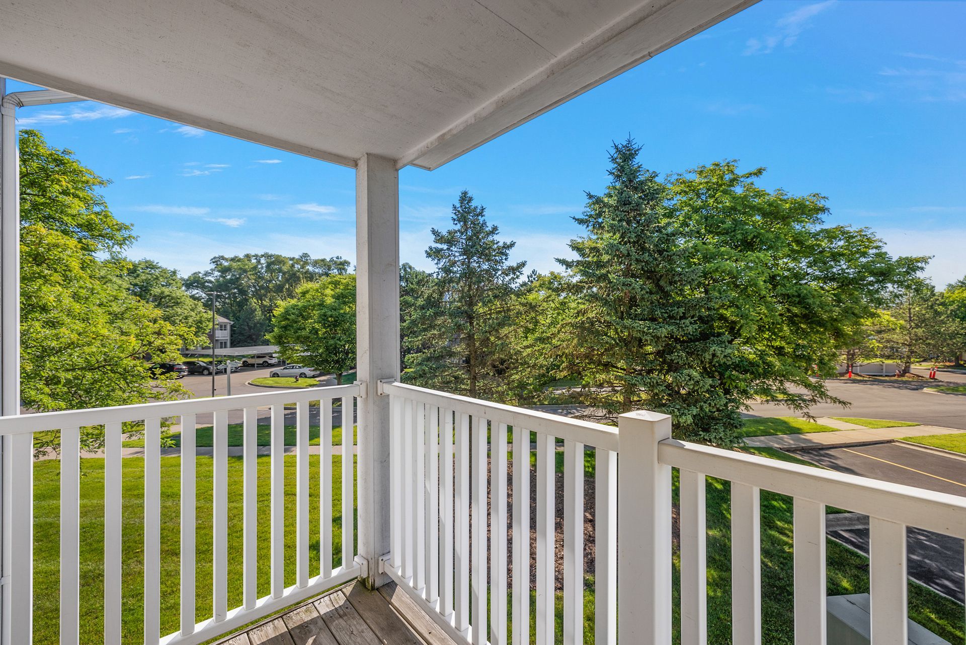 A balcony with a white railing overlooking a lush green field and trees.