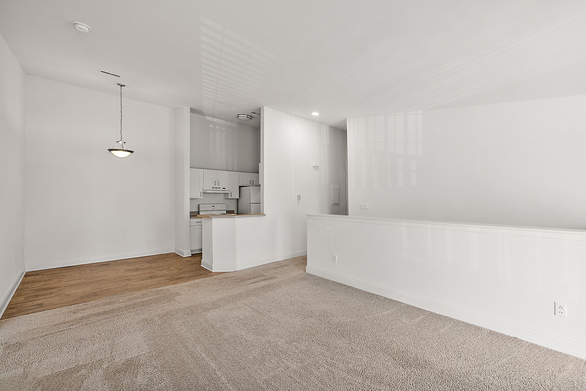 An empty living room with a carpeted floor and white walls.