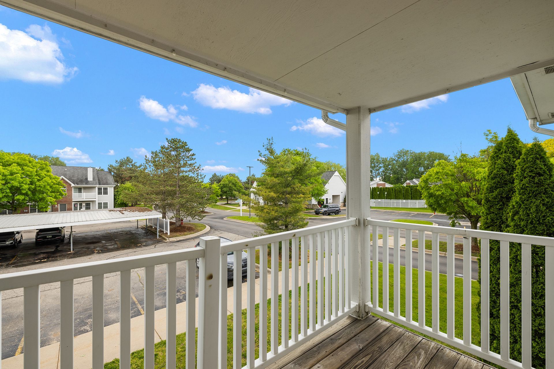 A balcony with a white railing overlooking a parking lot and a street.