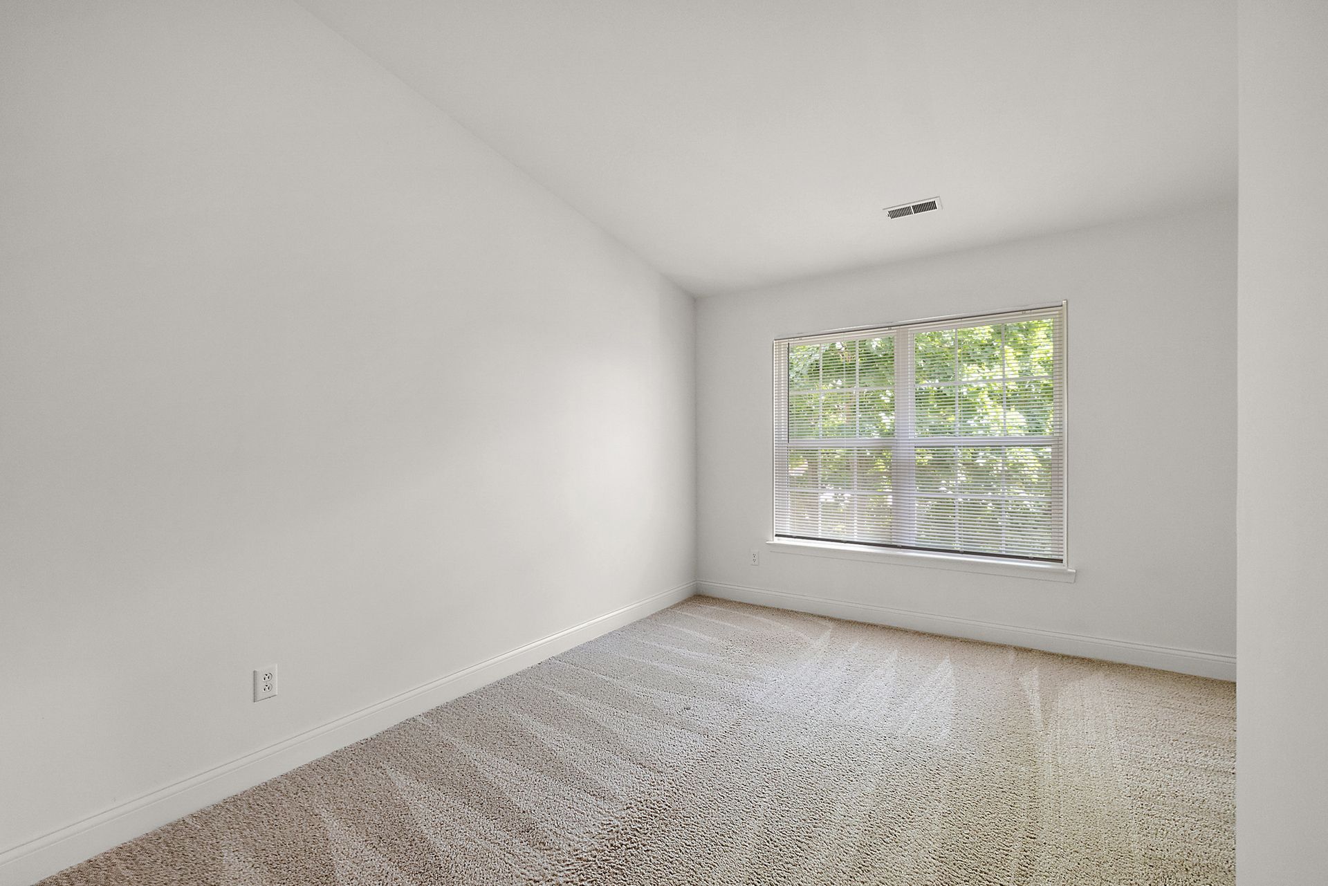 An empty bedroom with a window and carpet.