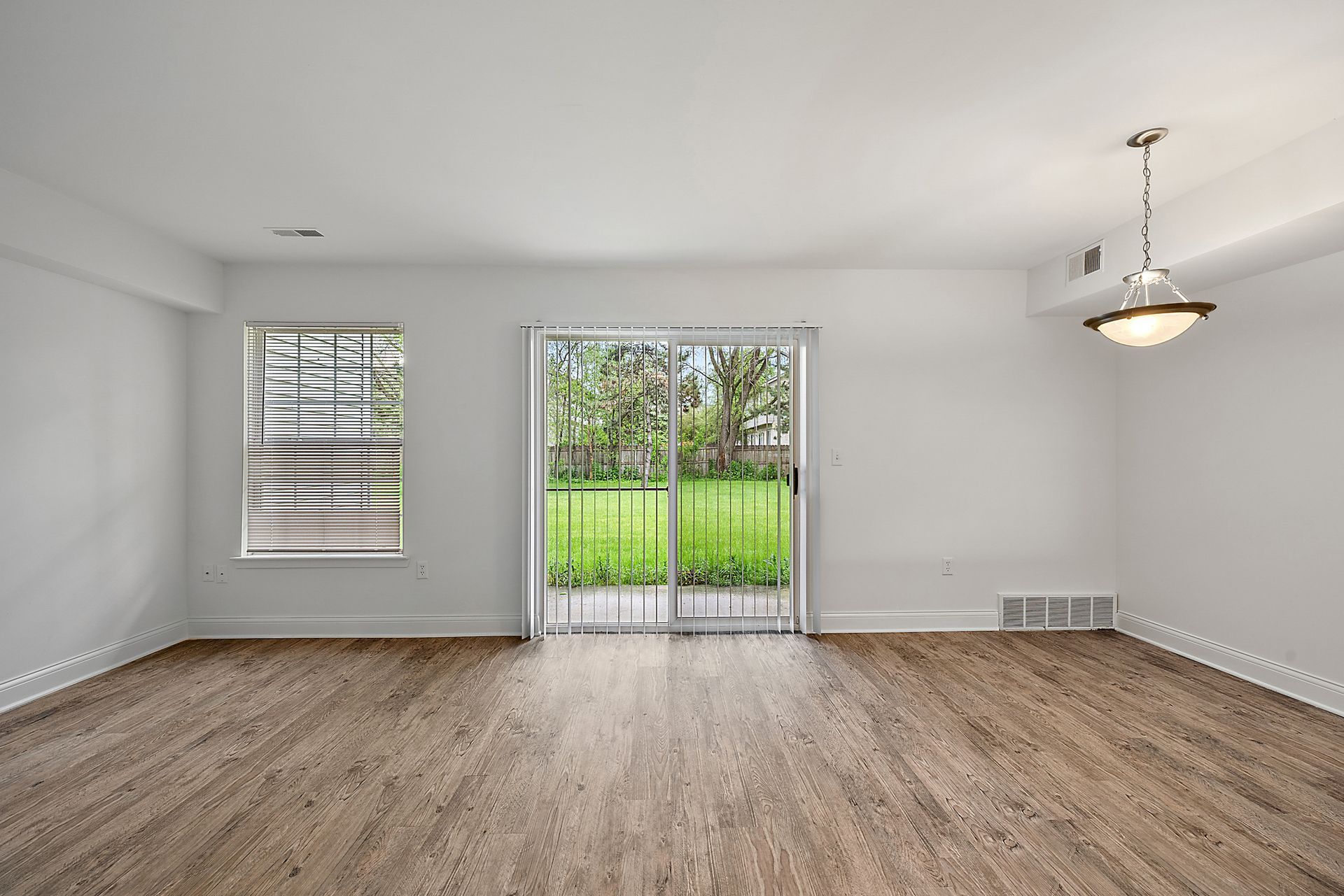 An empty living room with hardwood floors and sliding glass doors leading to a patio.