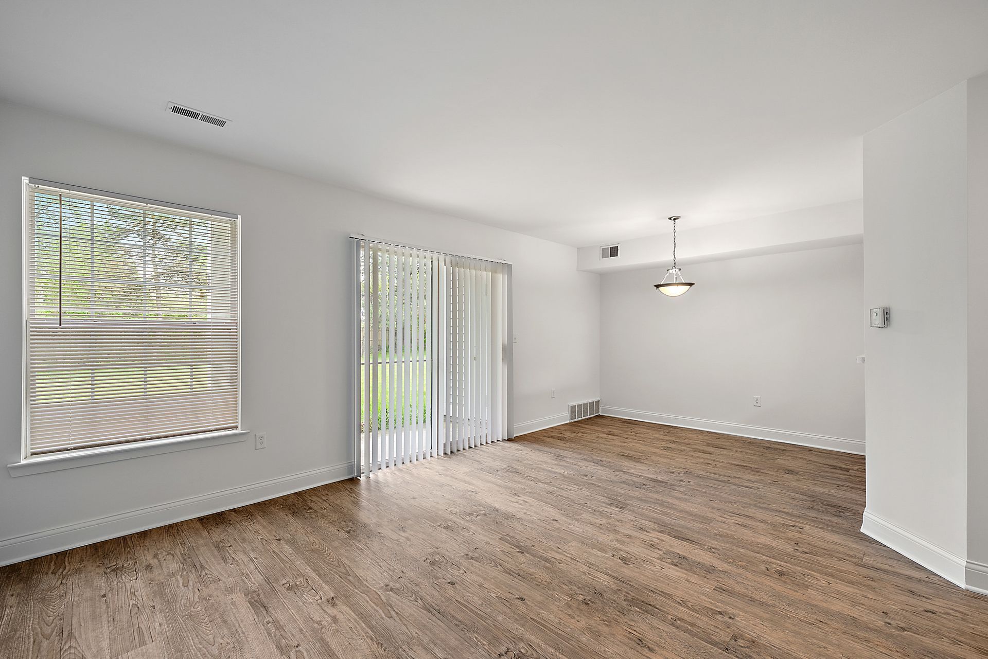 An empty living room with hardwood floors and sliding glass doors.