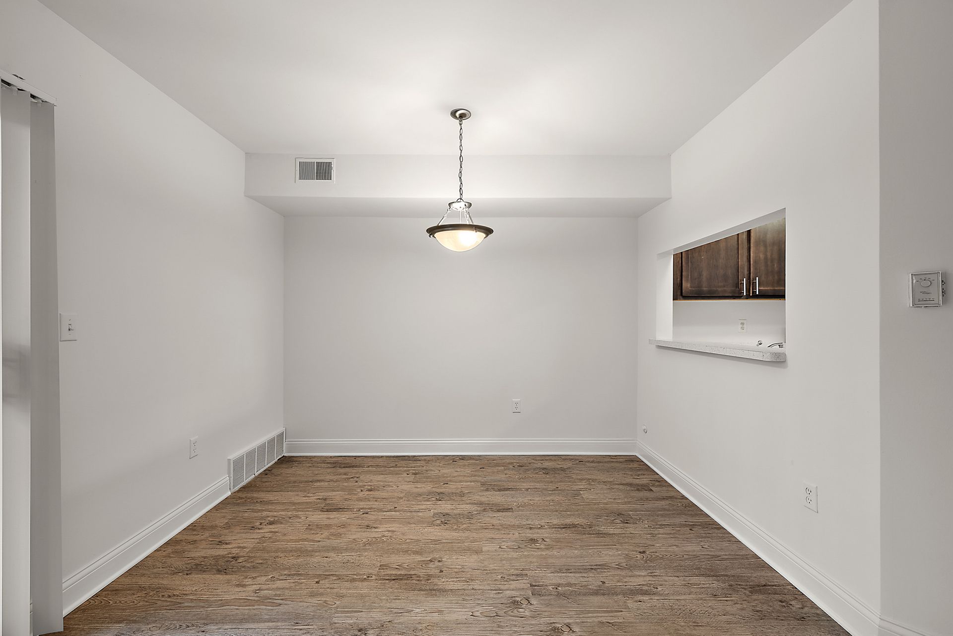 An empty dining room with wooden floors and white walls.