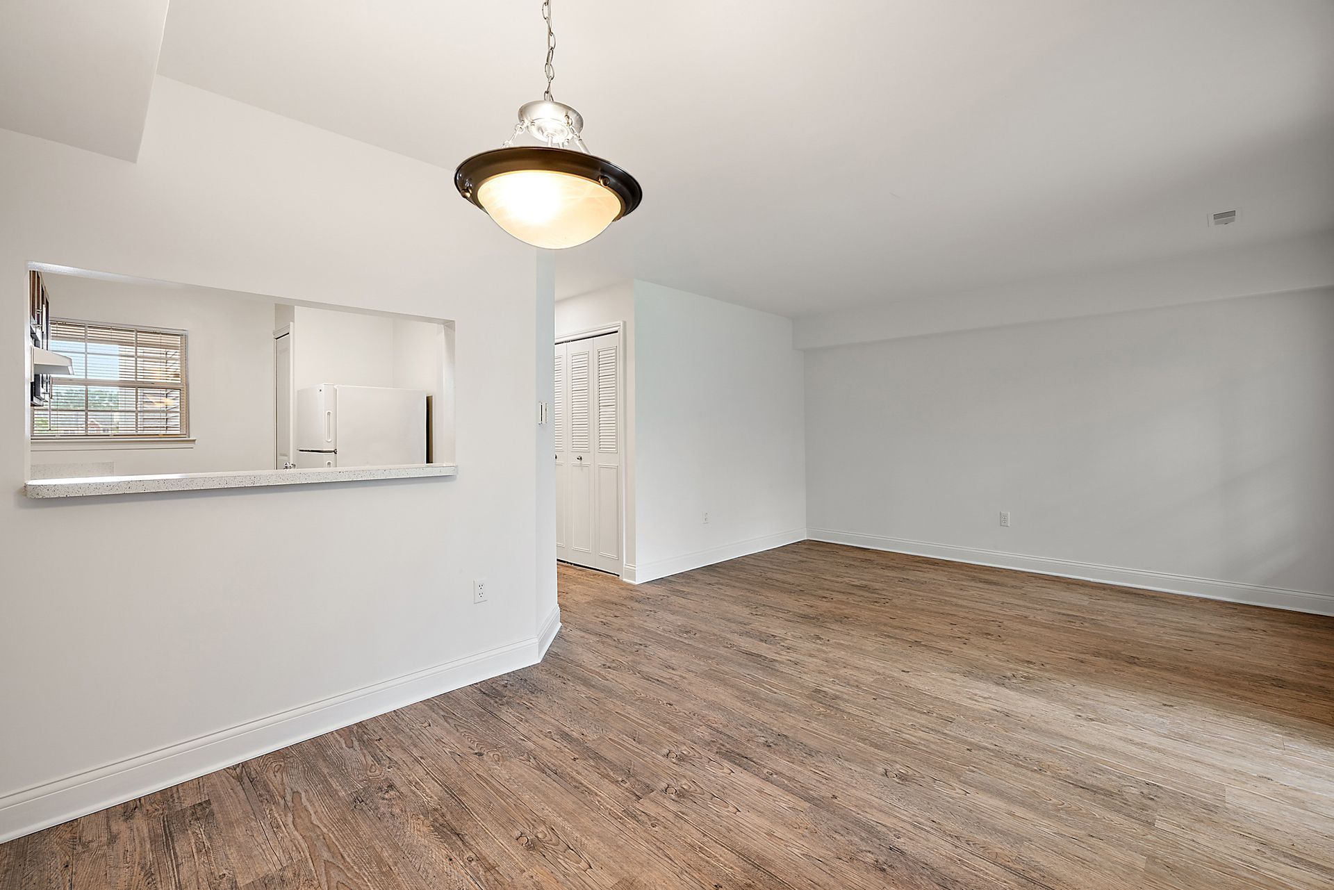An empty living room with hardwood floors and a chandelier hanging from the ceiling.