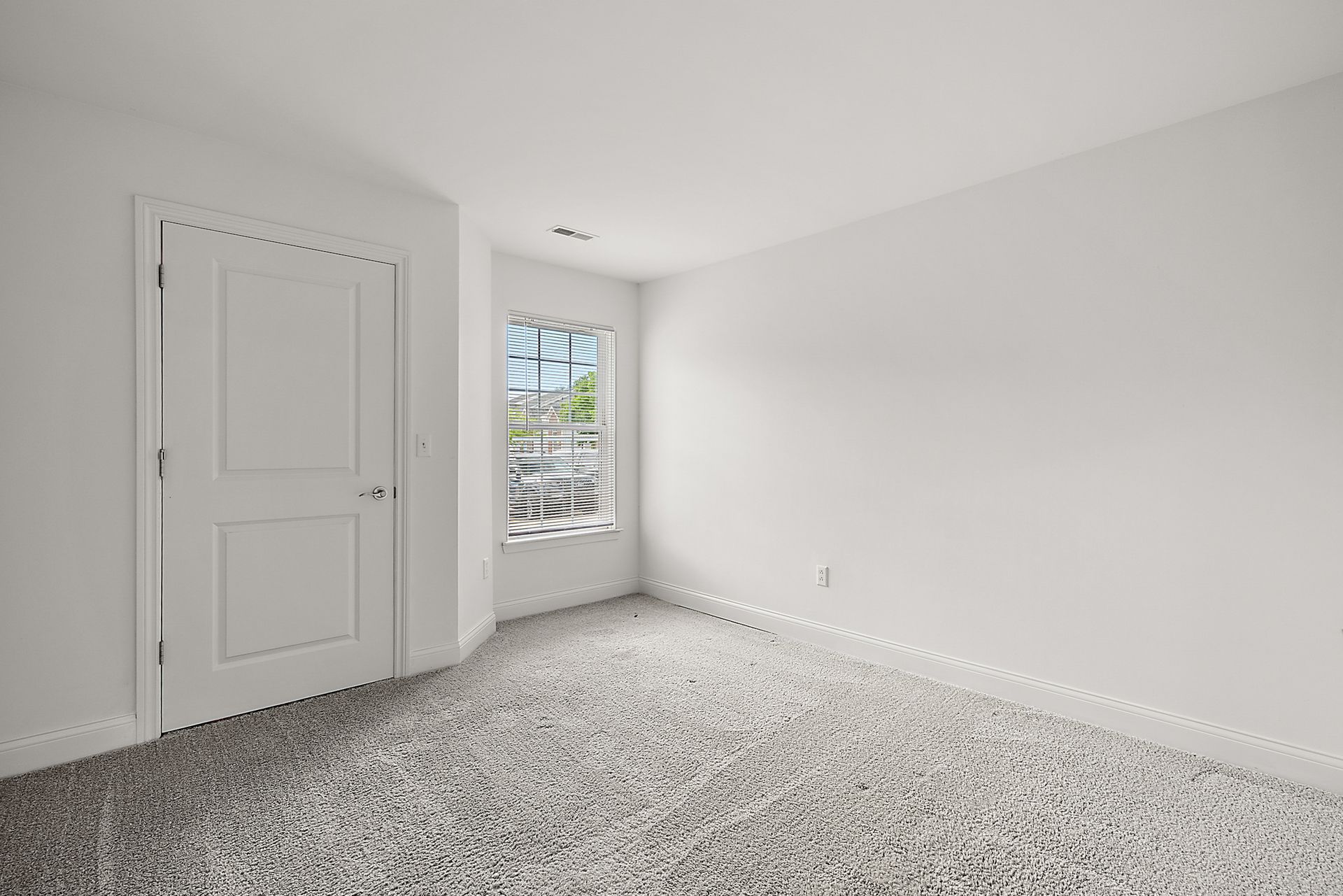An empty bedroom with a window and carpeted floor.