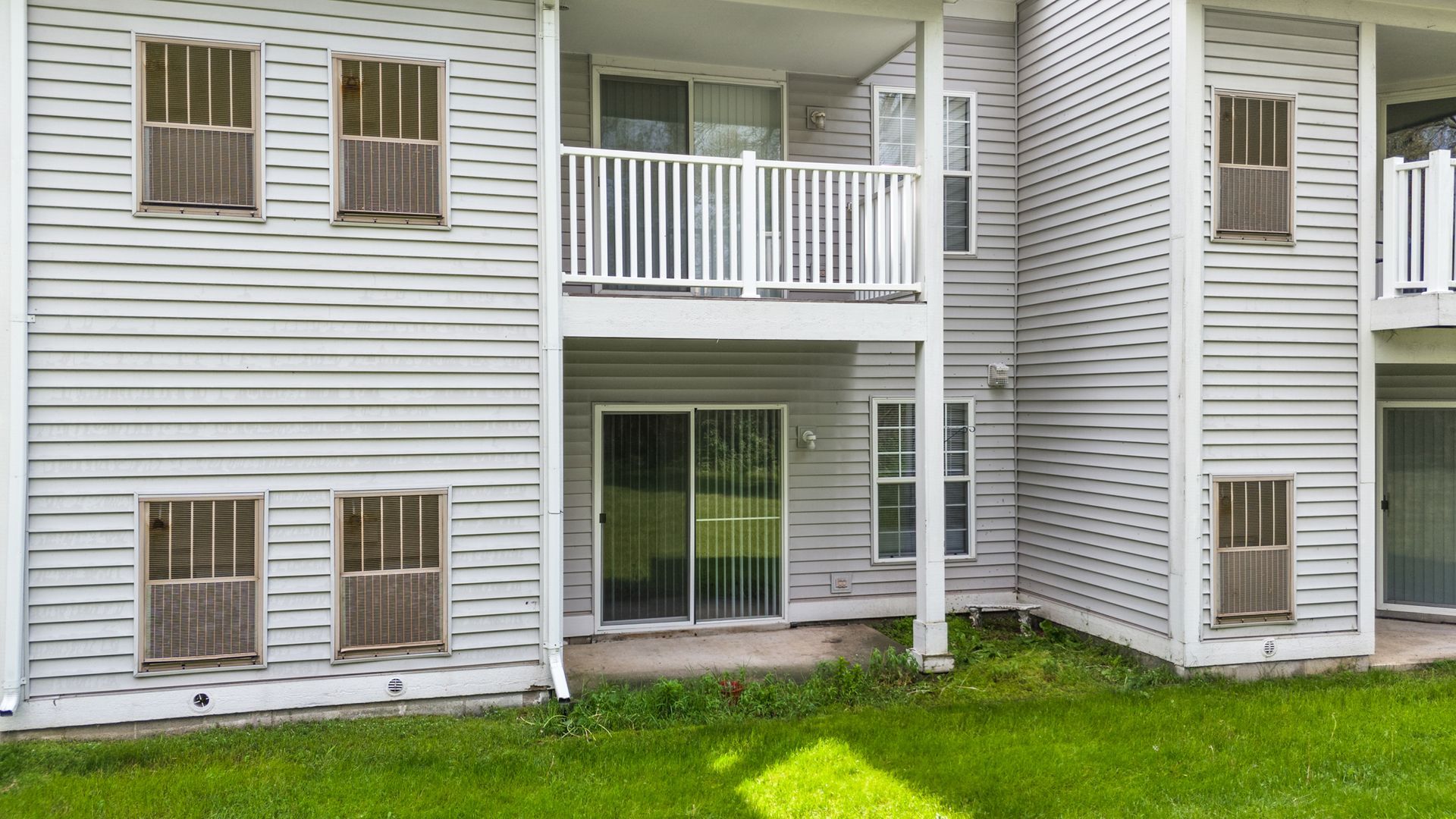 A white apartment building with a balcony and sliding glass doors.