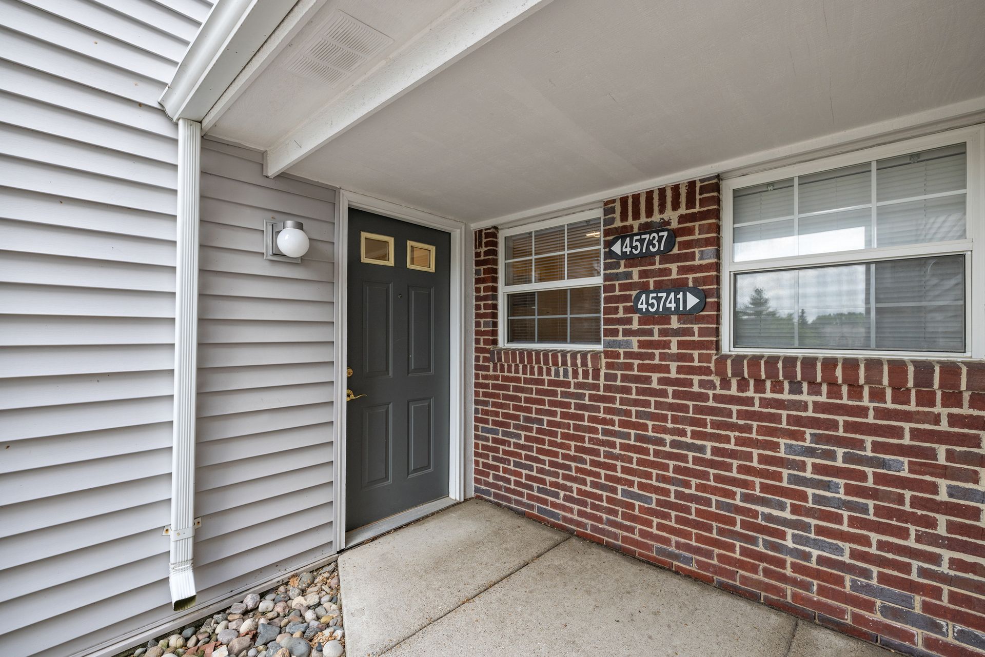 A brick house with a gray siding and a black door