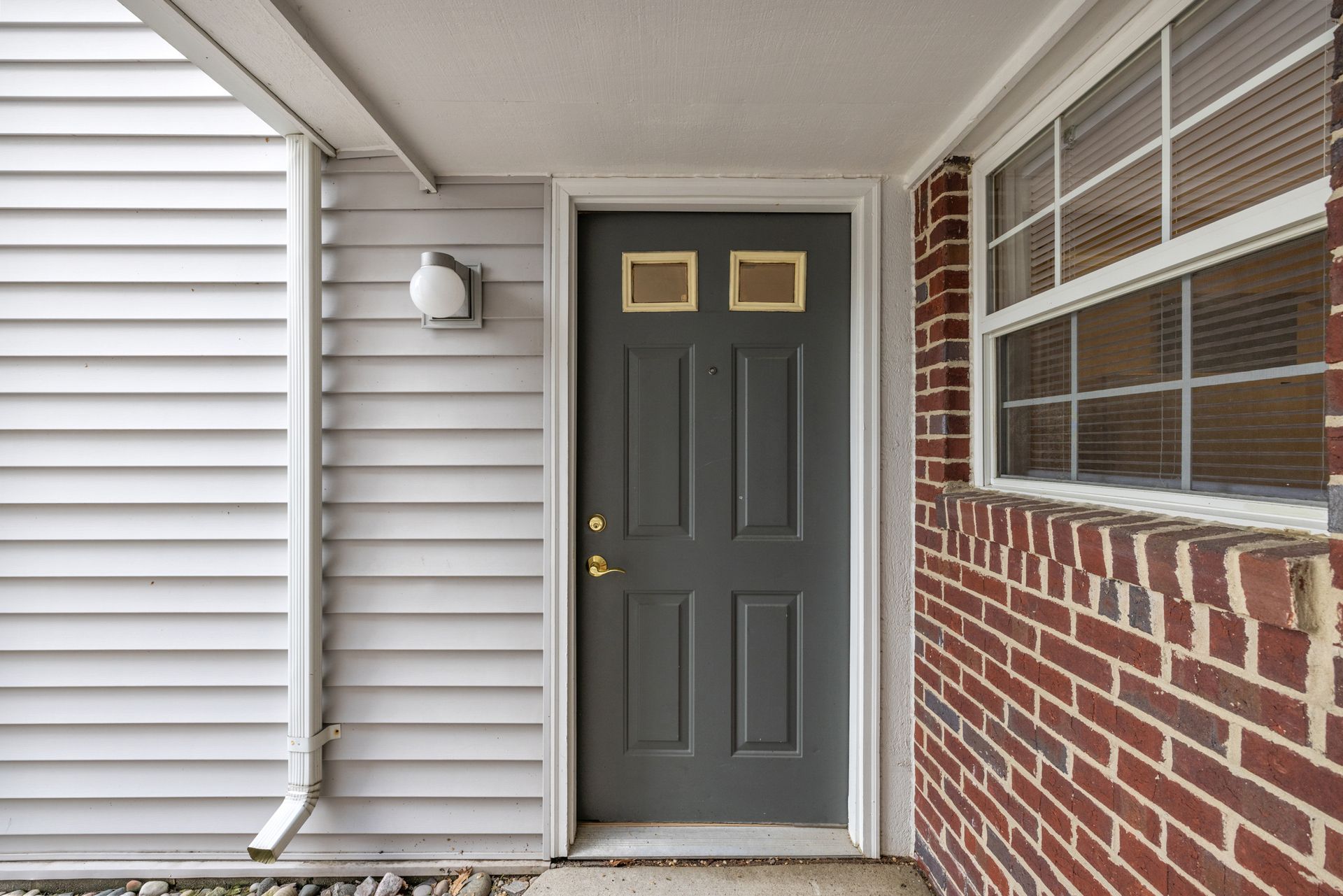 A brick house with a gray door and white siding