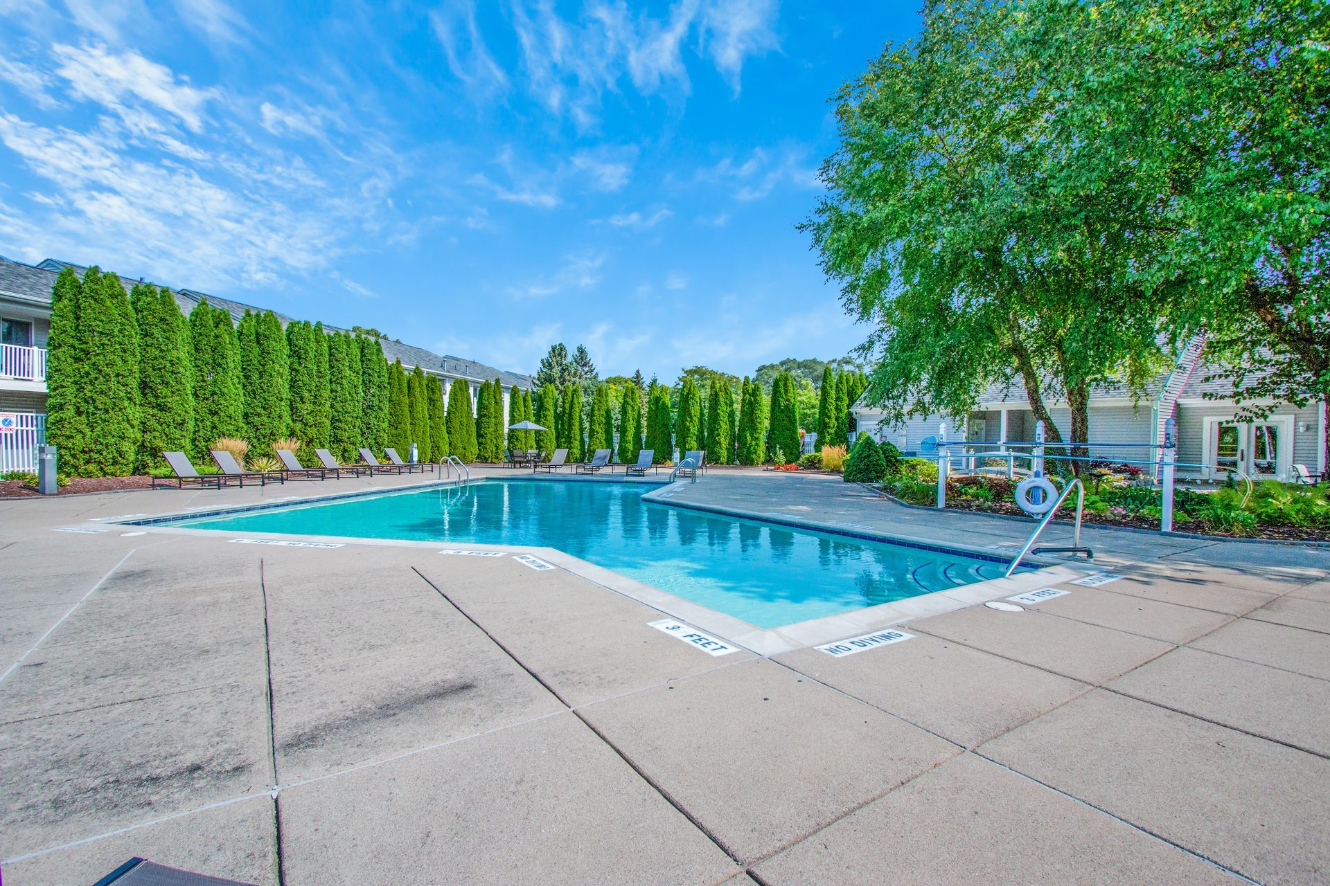 A large swimming pool is surrounded by trees and chairs.