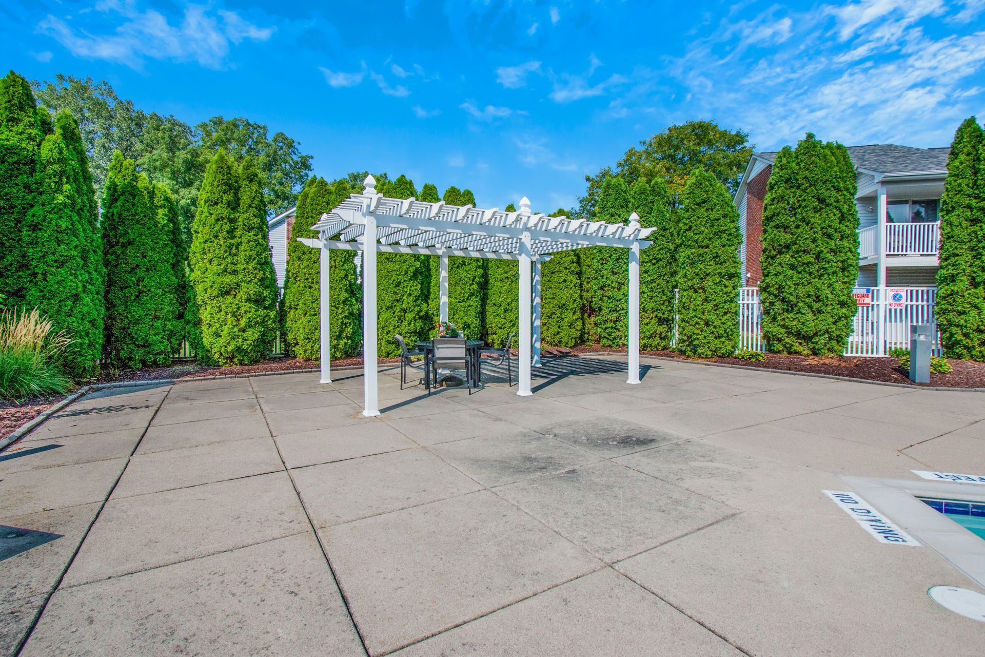 There is a pergola in the middle of a parking lot surrounded by trees.