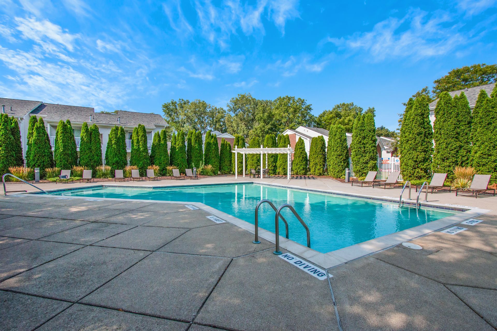 A large swimming pool surrounded by trees and chairs on a sunny day.