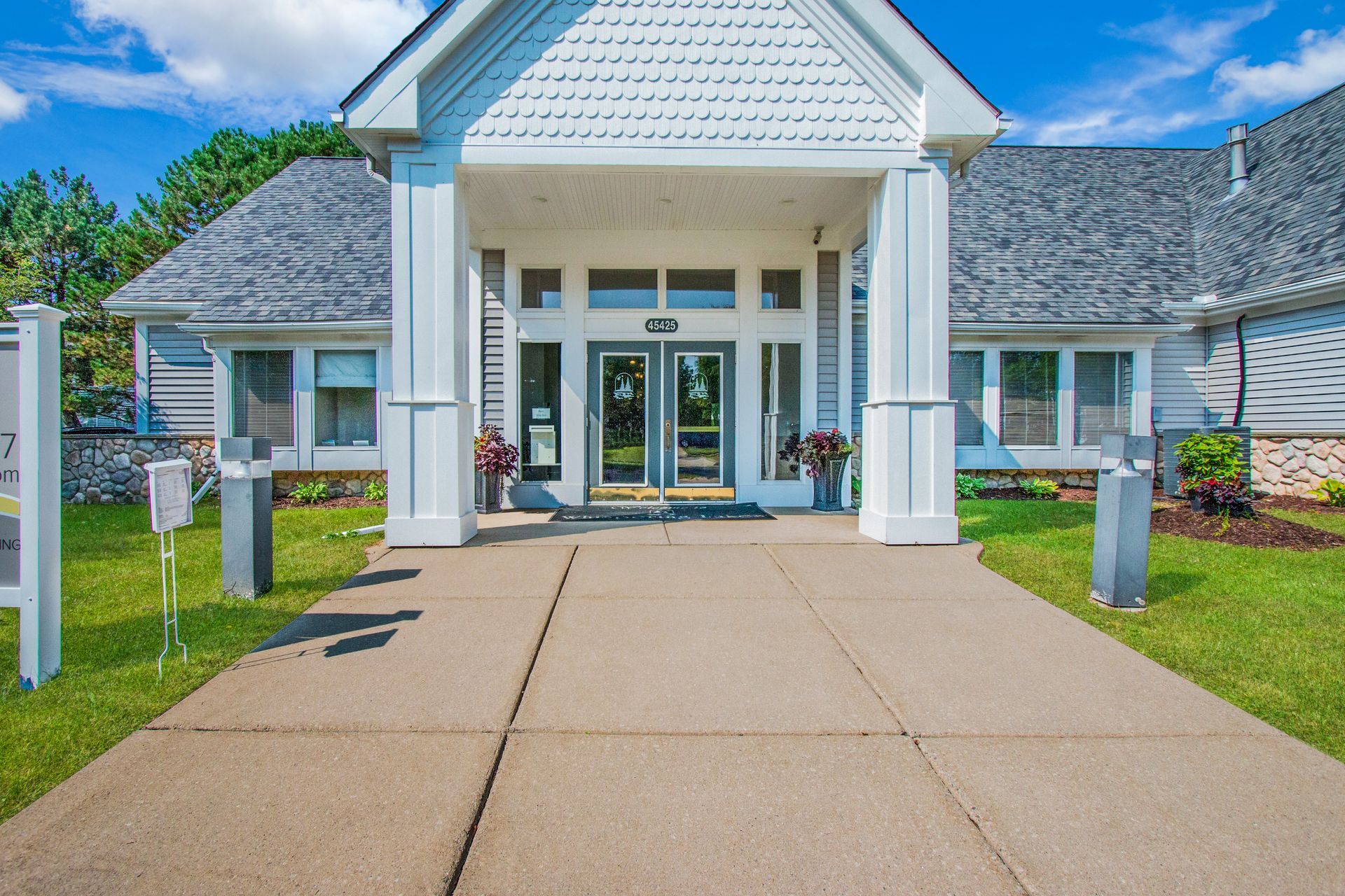 A white house with a gray roof and a concrete walkway leading to it.