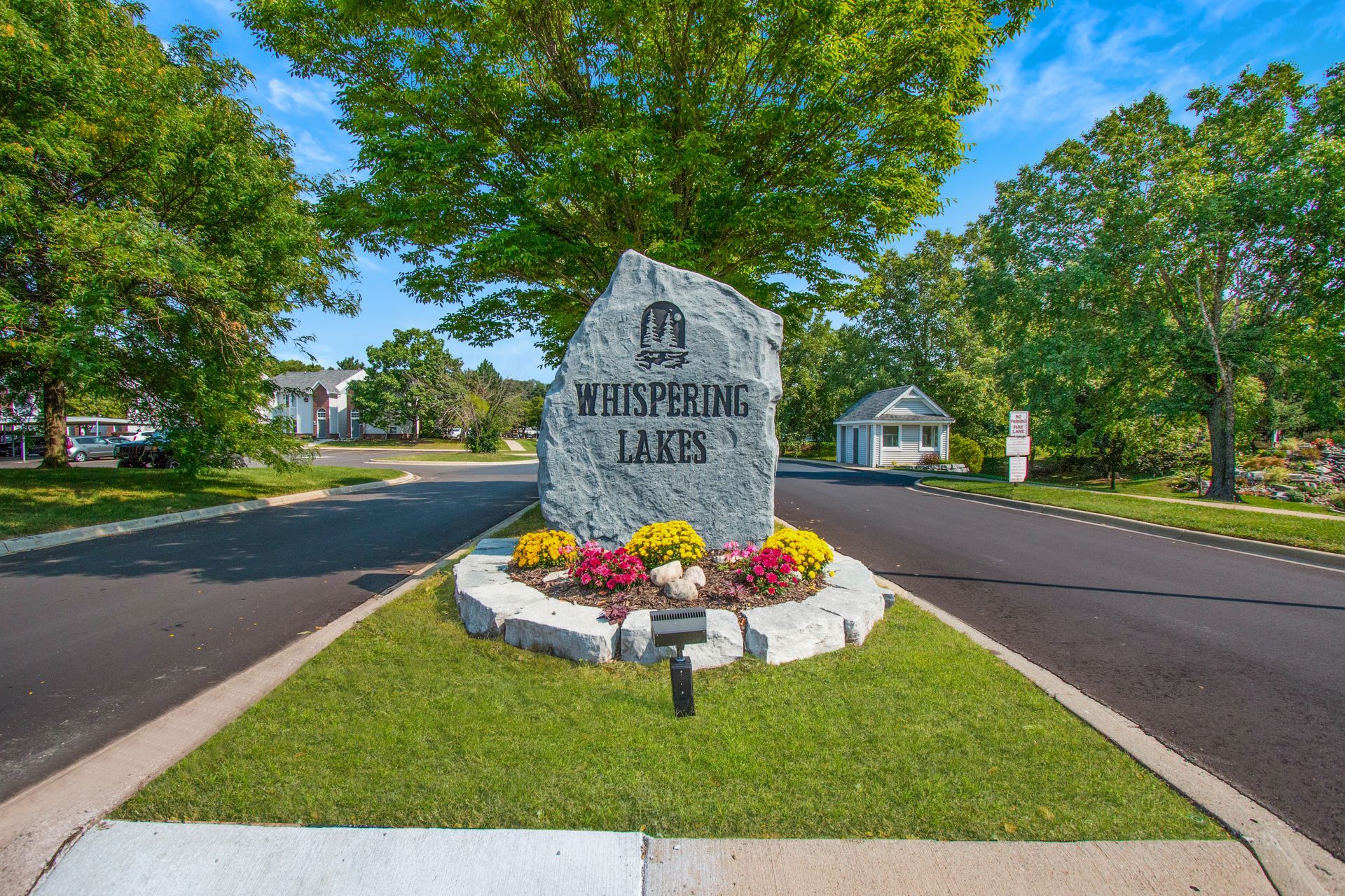 A sign for whispering lanes is sitting on the side of the road.