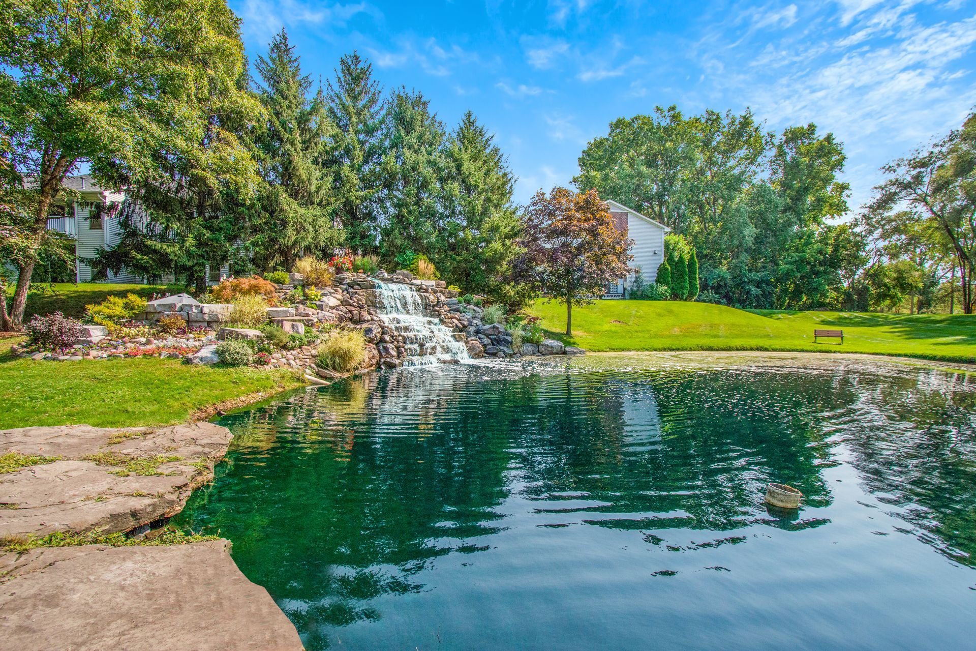 A pond with a waterfall in the middle of a park.