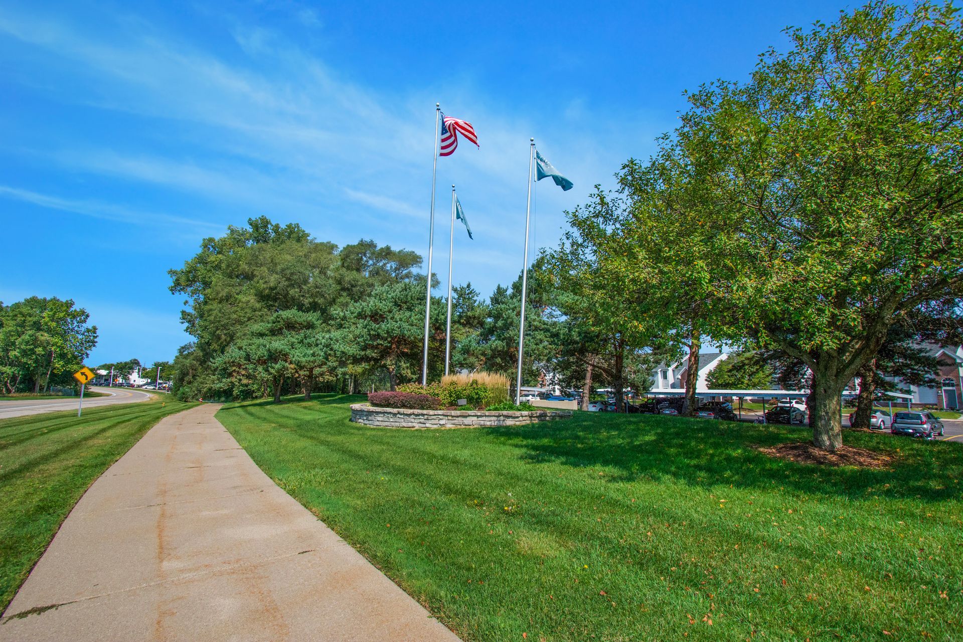 A concrete walkway going through a park with flags flying in the background.