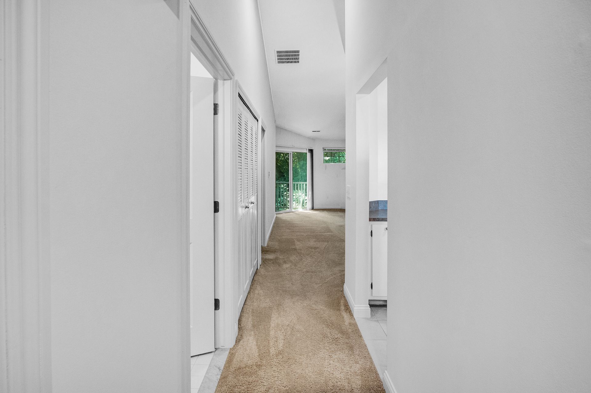A long hallway with a brown carpet and white walls in a house.