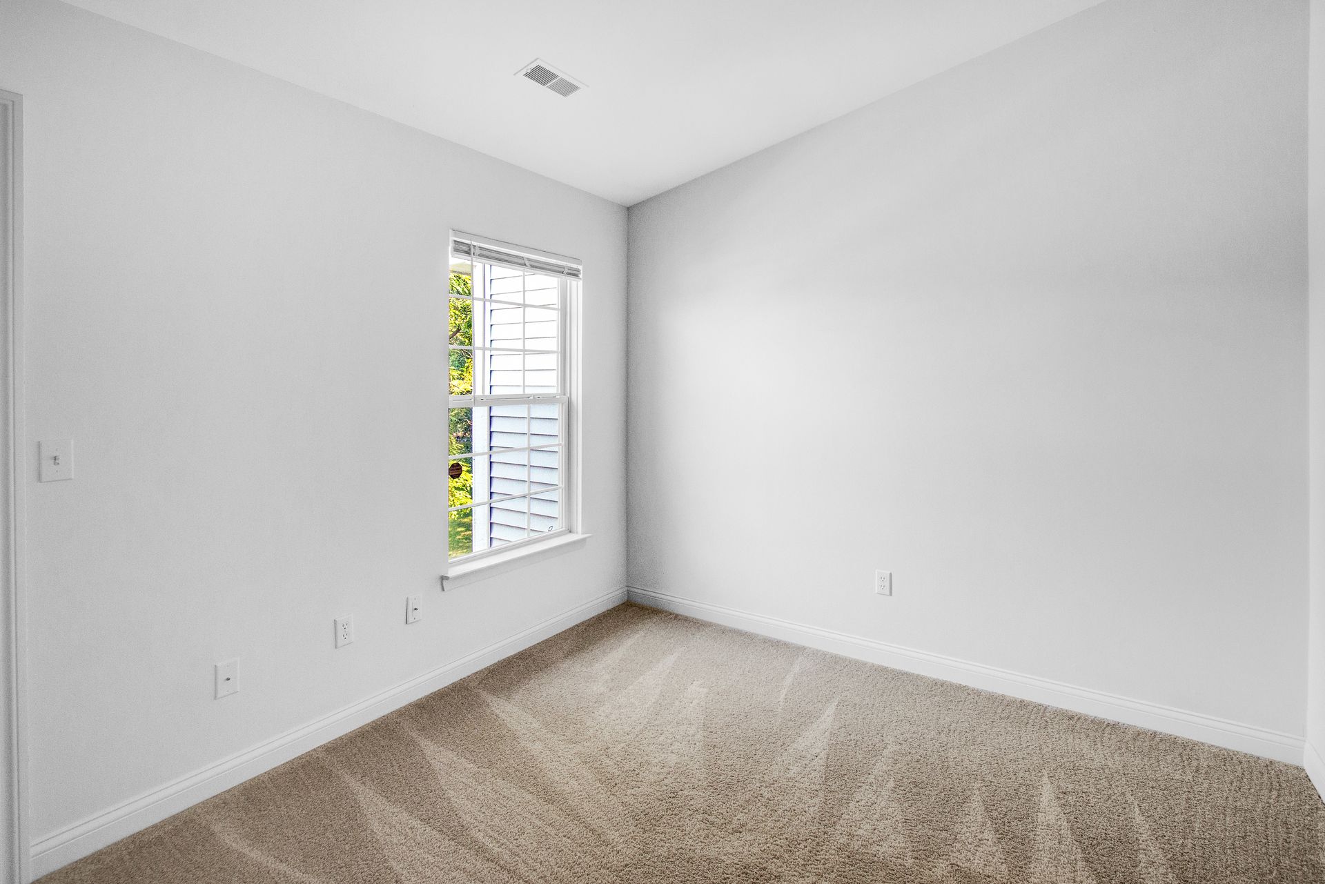 An empty bedroom with a window and carpet.
