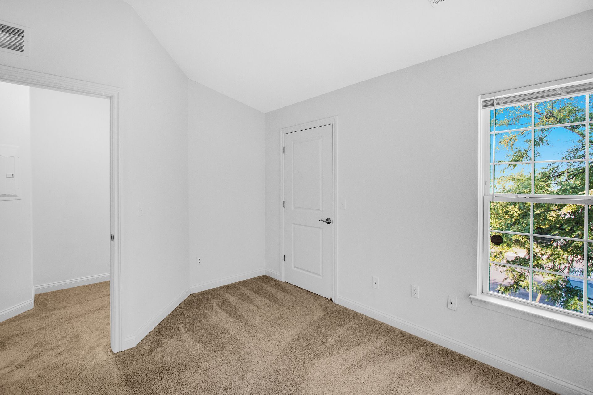 An empty bedroom with a window and a carpeted floor.