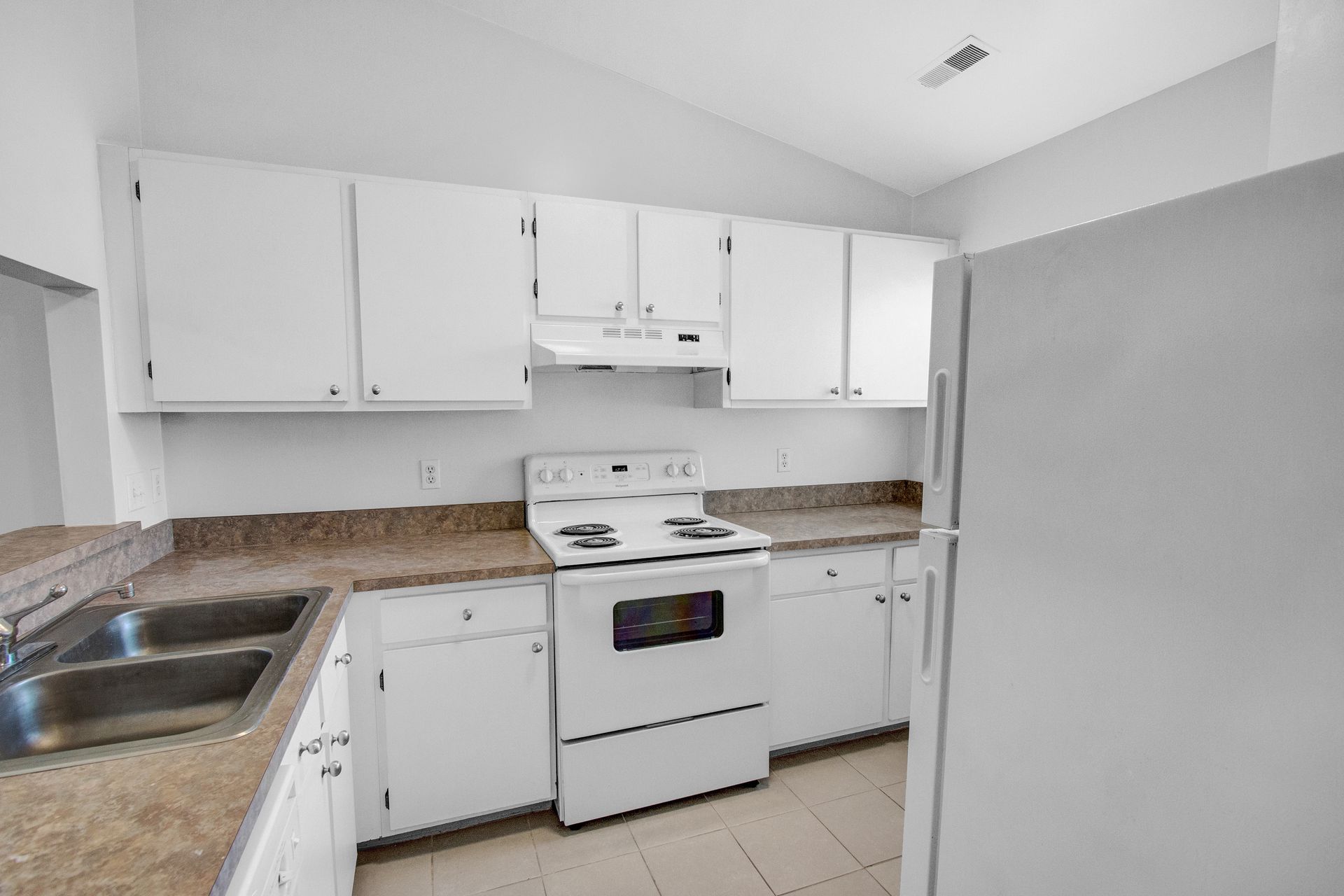 A kitchen with white cabinets , a stove , a refrigerator and a sink.