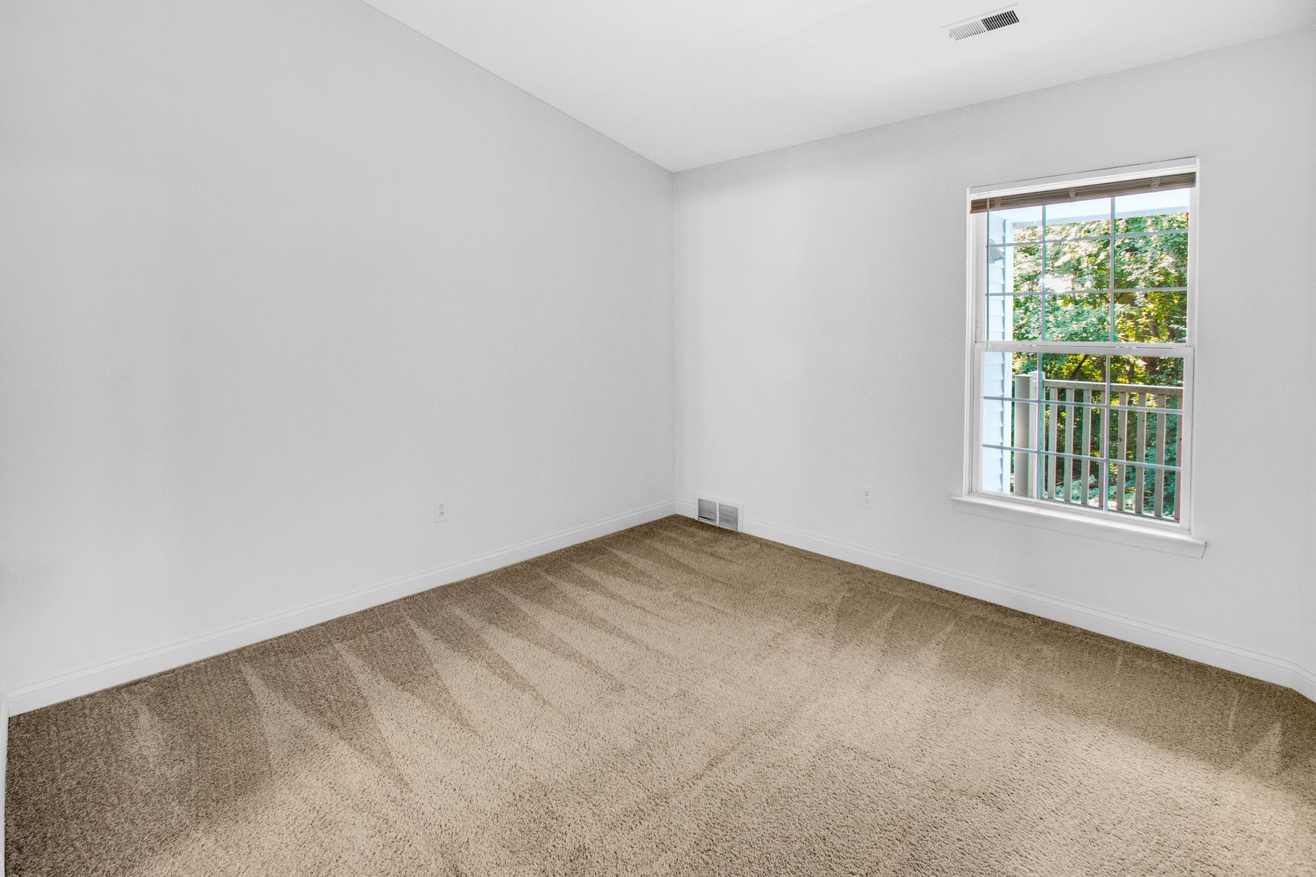 An empty bedroom with a window and carpet.