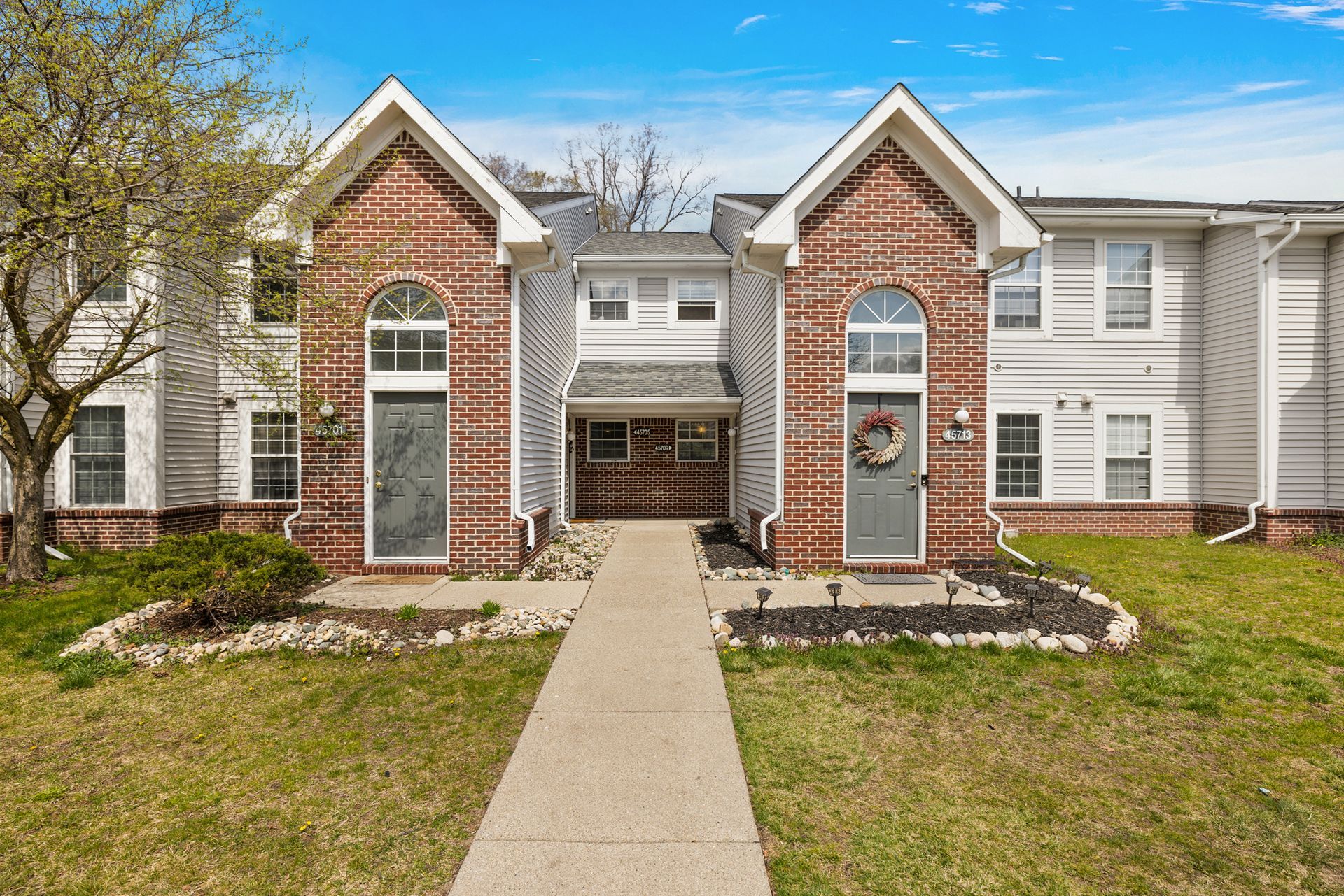 A brick and white house with a concrete walkway leading to it.
