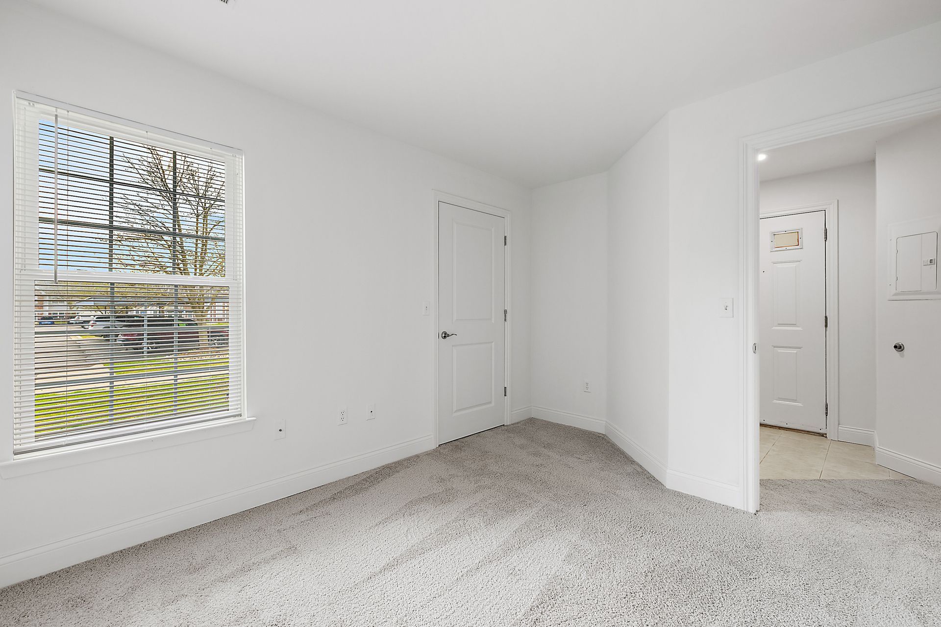 An empty bedroom with a window and a carpeted floor.