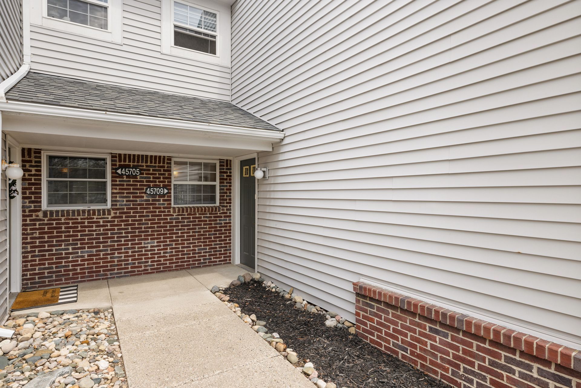 A brick house with a white siding and a walkway leading to it.
