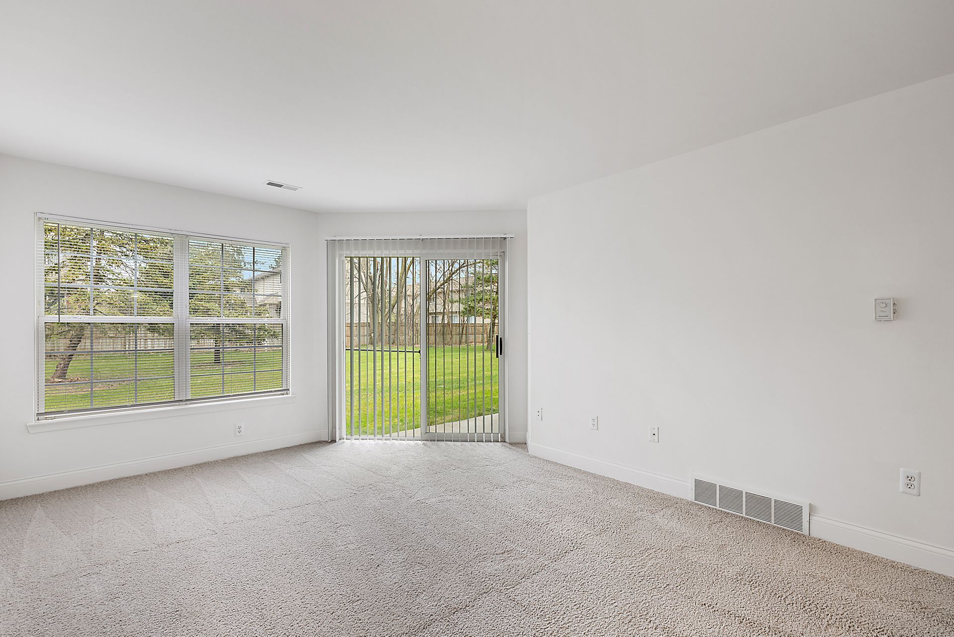 An empty living room with a sliding glass door and a large window.