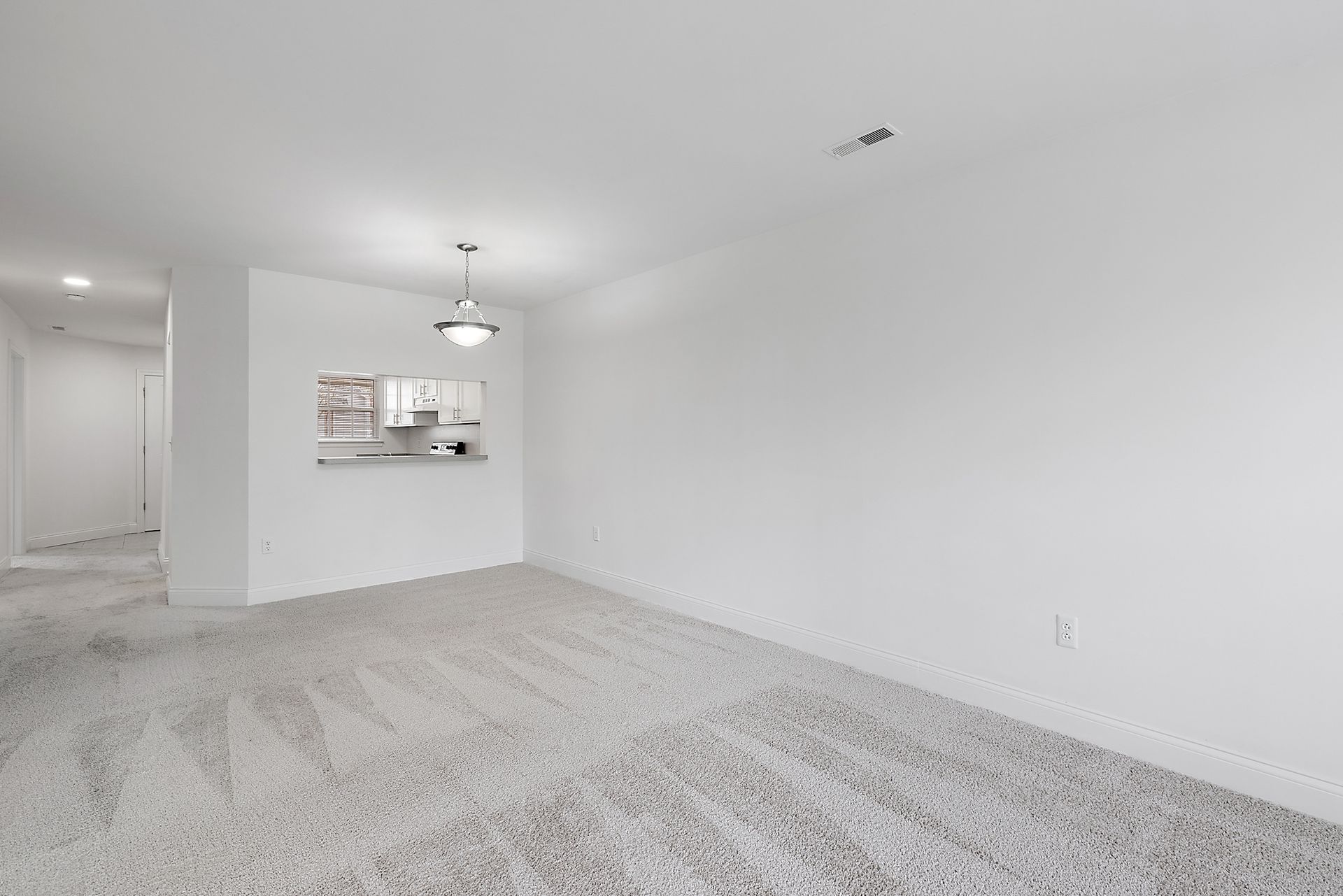 An empty living room with a carpeted floor and white walls.