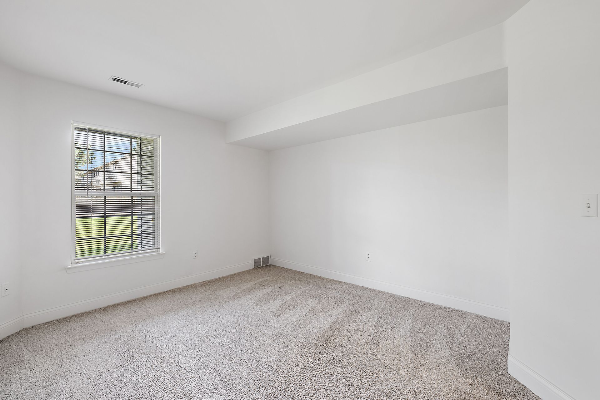 An empty bedroom with a window and a carpeted floor.