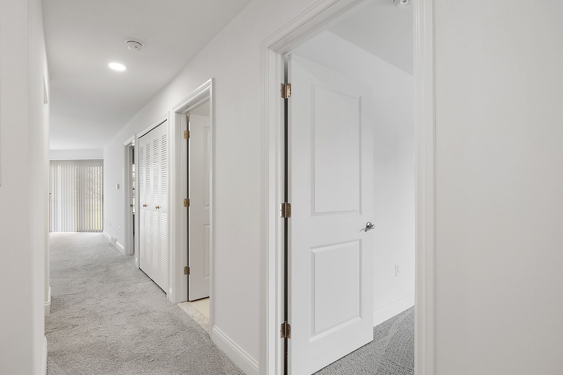 A hallway in a house with white walls and a carpeted floor.