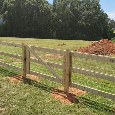 A wooden fence with a gate in the middle of a grassy field.