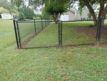 A chain link fence is in the middle of a lush green field.