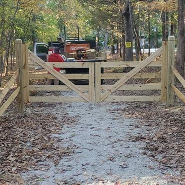 A wooden gate is sitting on the side of a dirt road in the woods.