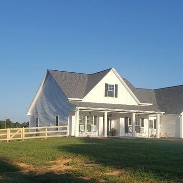 A white house with a porch and a fence in front of it.