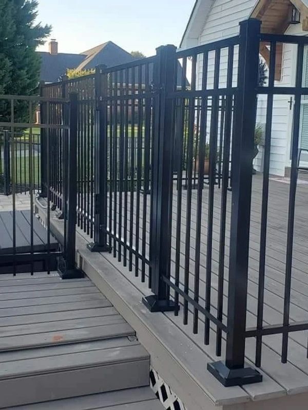 A black fence surrounds a wooden deck in front of a house.