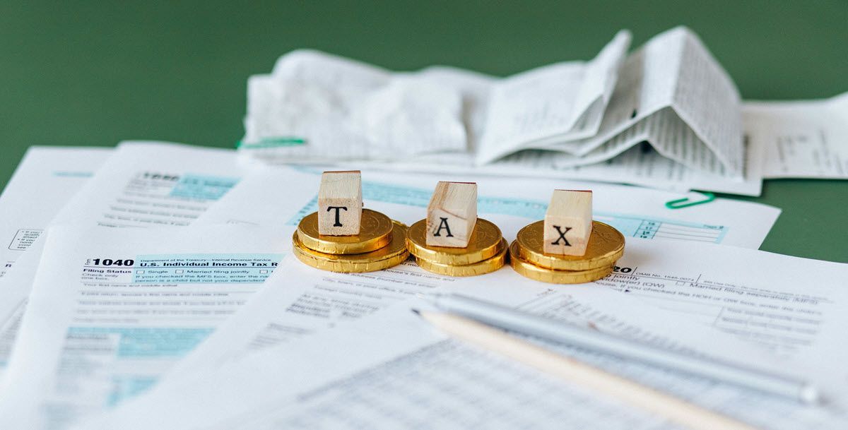 Tax documents with coins and a pen, the coins spelling 