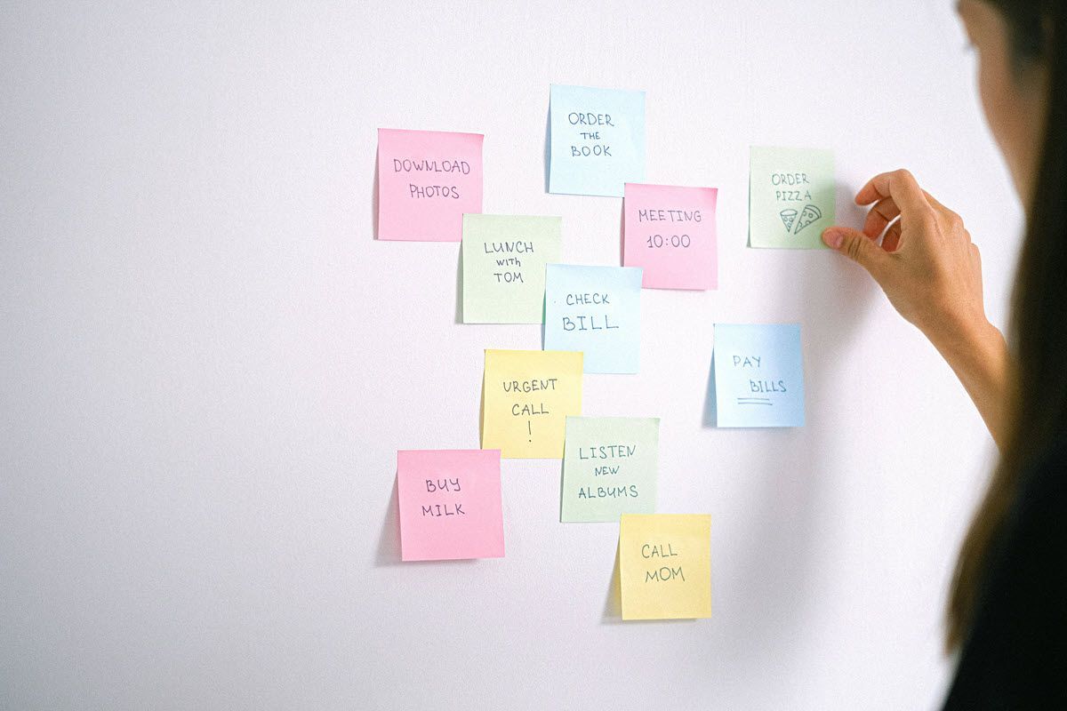 Woman arranging colorful sticky notes on a white wall, brainstorming ideas.