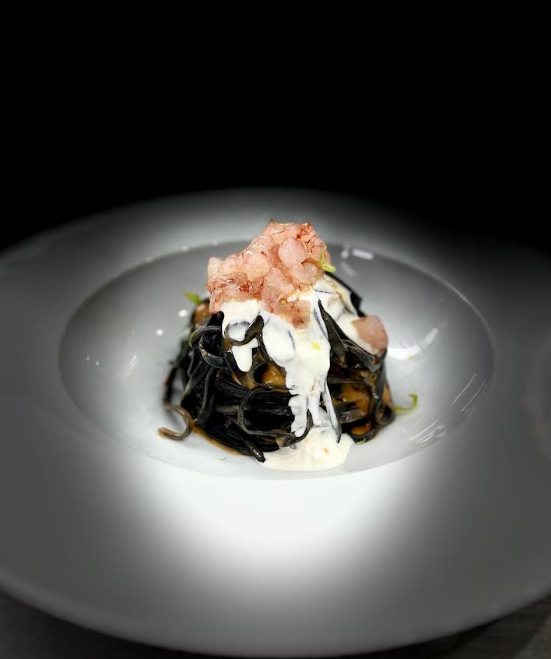 Un piatto bianco con sopra tagliatelle e gamberetti su un tavolo.