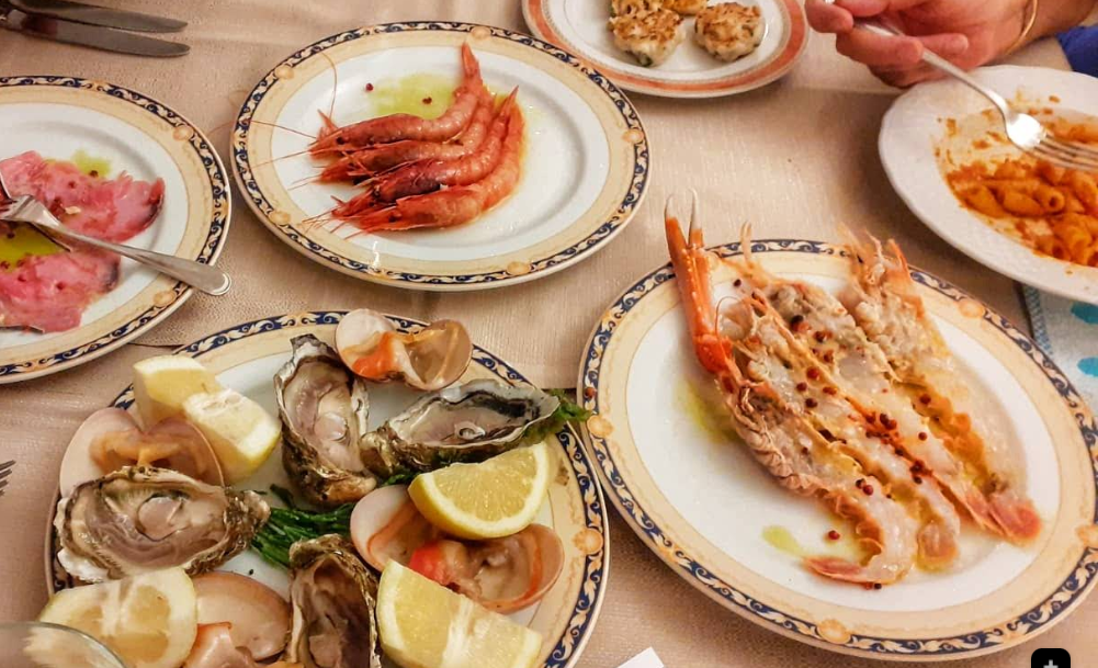 Un tavolo sormontato da piatti di cibo tra cui gamberi e ostriche