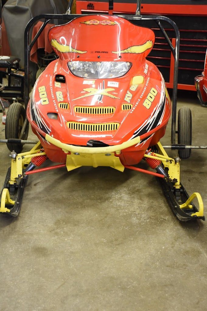 A red and yellow snowmobile is parked in a garage