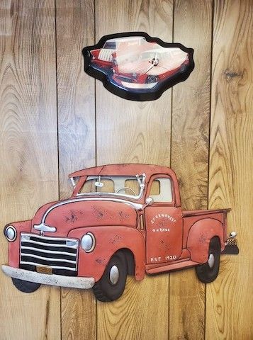 A red truck is sitting on a wooden wall next to a picture of a car.