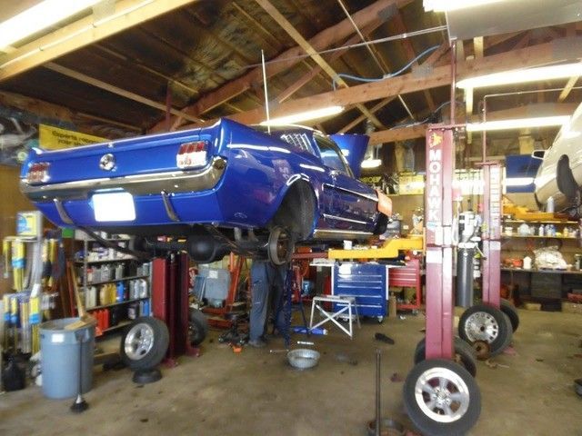 A blue mustang is on a lift in a garage