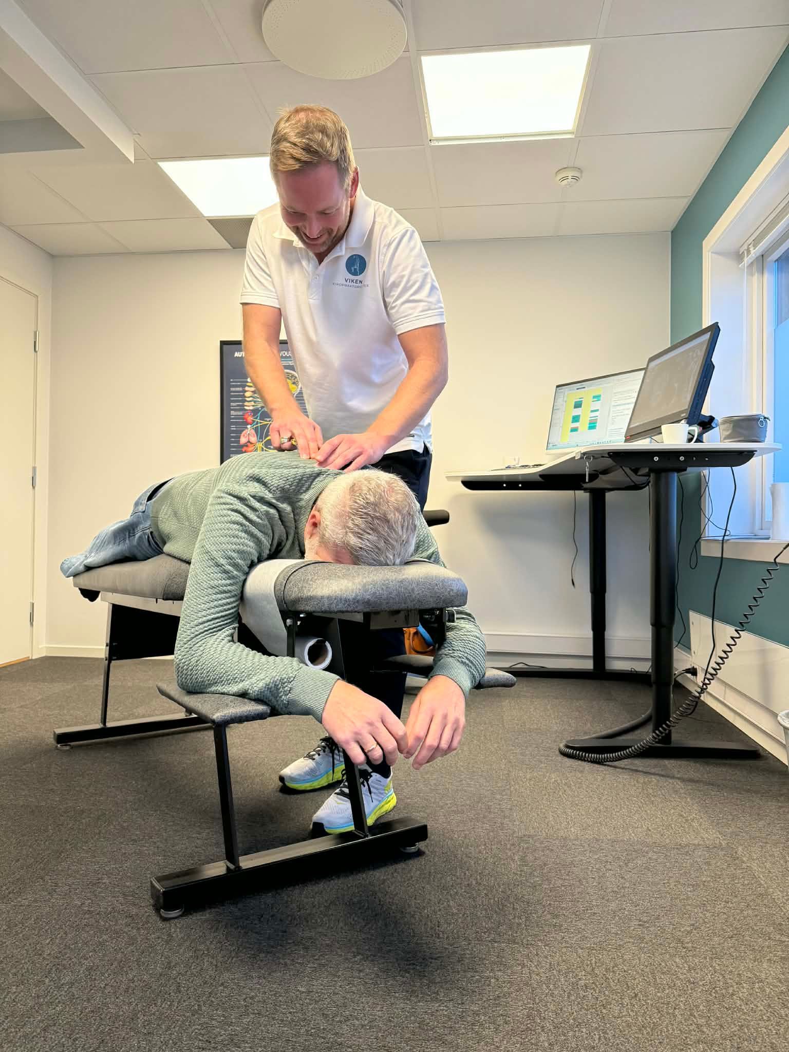 Mann gir ryggmassasje til en person som sitter i en spesialstol på et kontor.