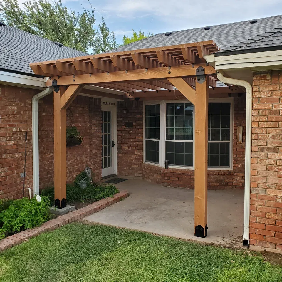 a wooden pergola is attached to the side of a brick house .